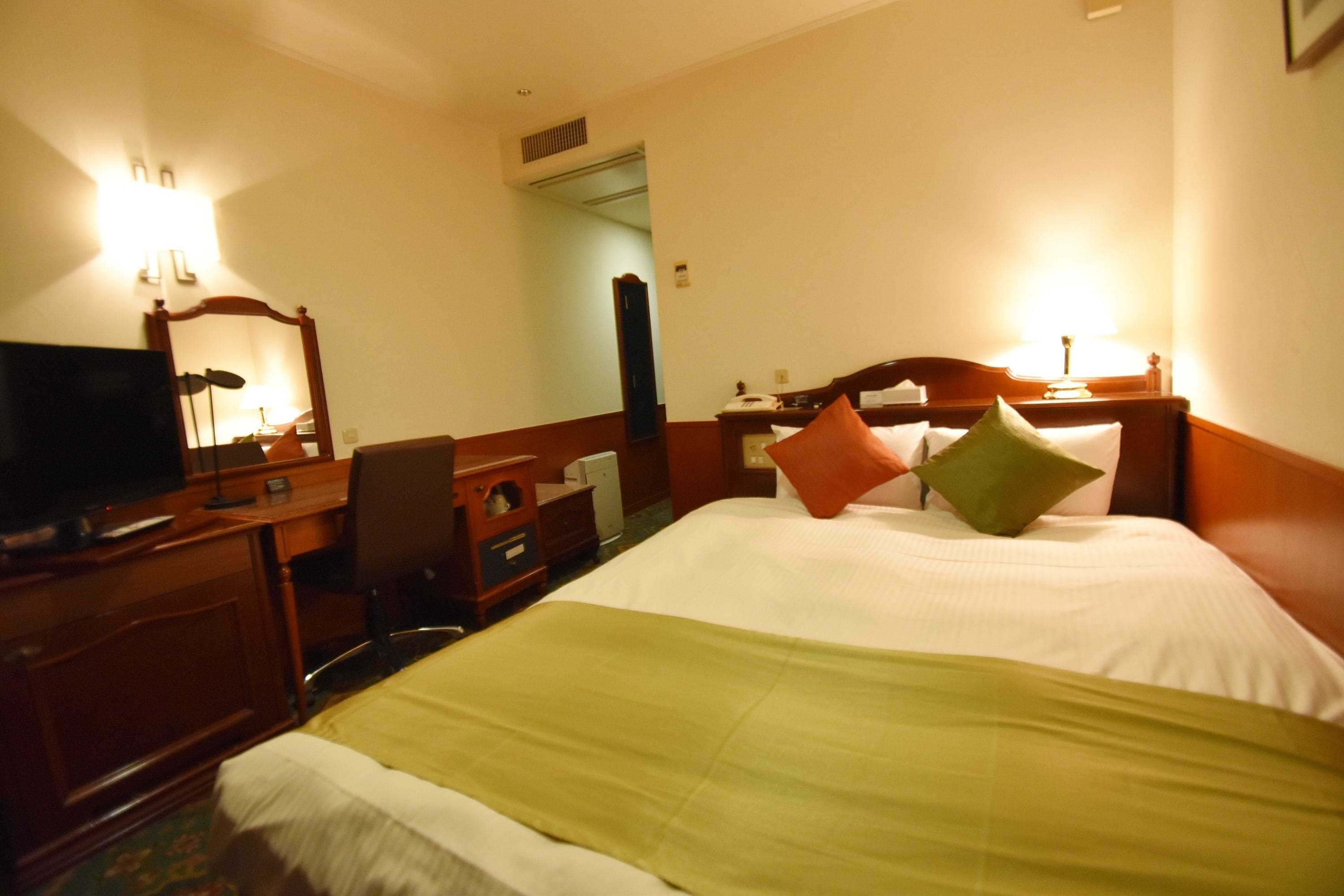 Una habitación de hotel con cama, escritorio, televisor y espejo.