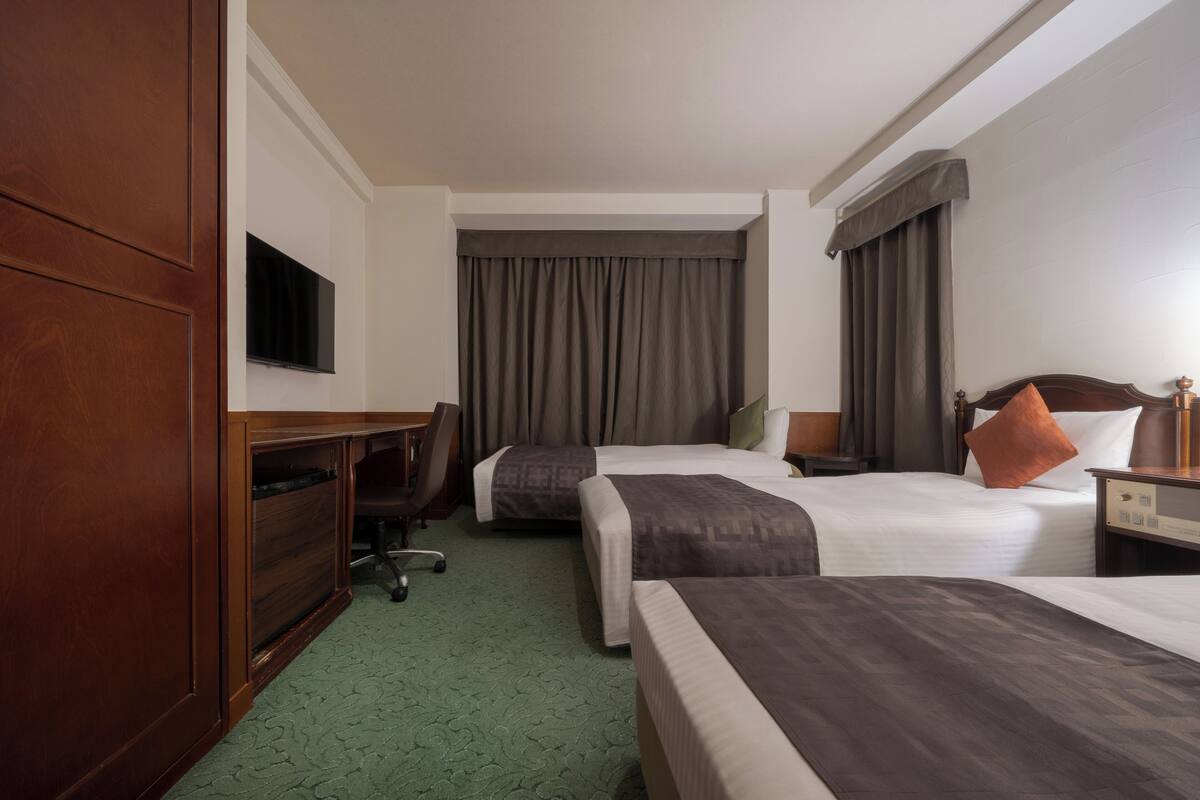 Habitación de hotel con dos camas, un escritorio, una silla, un televisor y una mesita de noche con lámpara.
