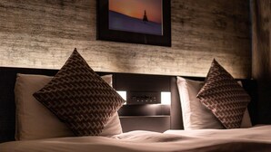 Une chambre d’hôtel avec un lit, deux coussins à motifs, une tête de lit et un tableau encadré au mur.