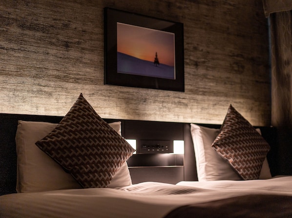 Habitación de hotel con una cama, dos almohadas estampadas, cabecera y un cuadro enmarcado en la pared.