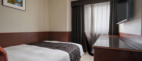 A hotel room with a bed, a desk, a chair, a TV, and a window with curtains.