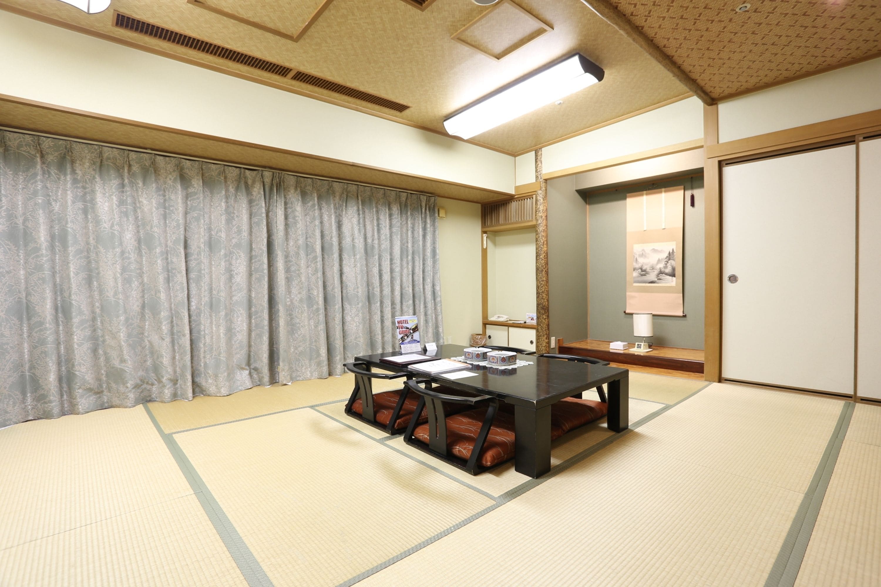 Um quarto japonês tradicional com piso de tatame, uma mesa baixa com almofadas, uma janela grande com cortinas e uma porta deslizante.