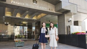 L’extérieur du Premier Hotel – une cabane avec une entrée en verre, un jardinier et un panneau indicateur.