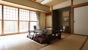 Une pièce de style japonais traditionnel, avec un sol recouvert de tatamis, une petite table basse avec des coussins, une porte coulissante et une grande fenêtre avec des stores.