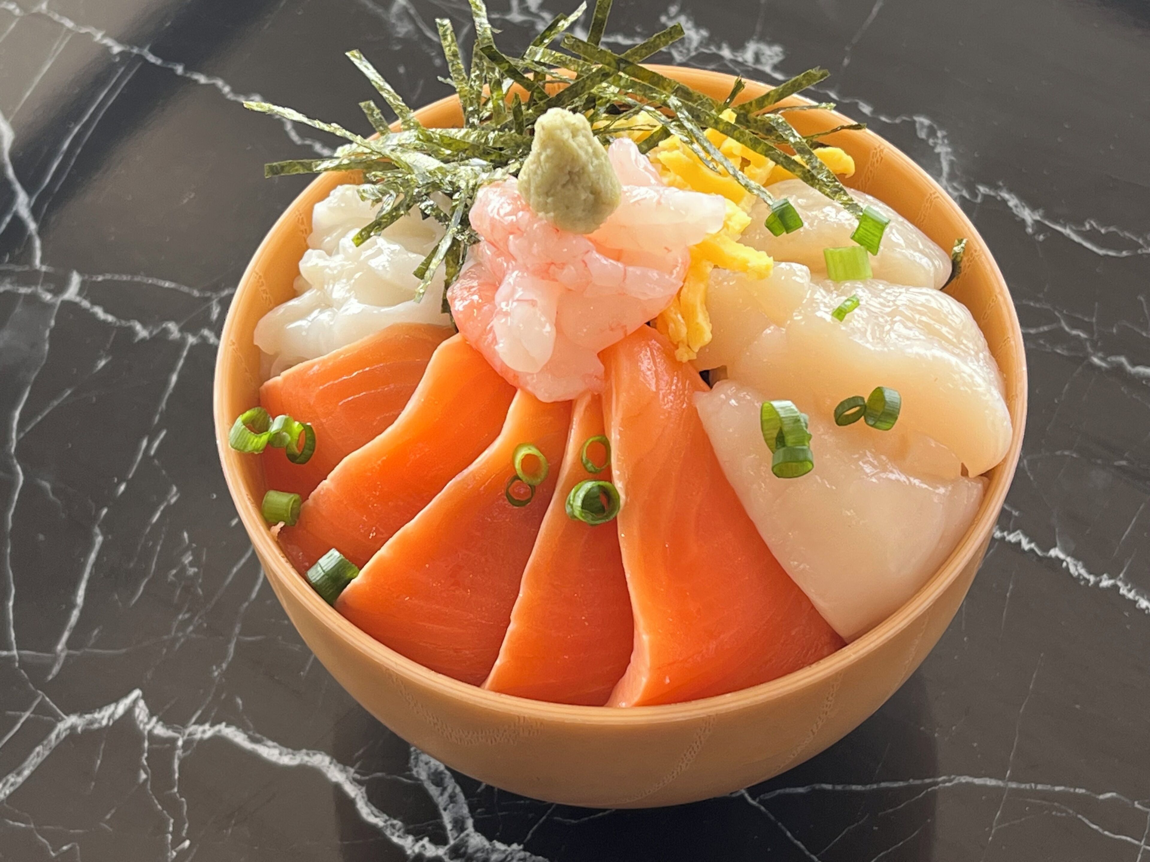 A bowl of sashimi with salmon and other fish, garnished with green onions and seaweed.