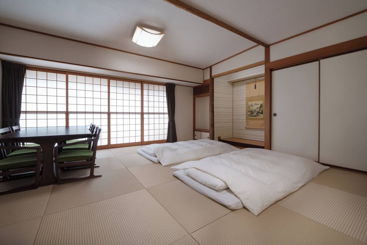 Una habitación japonesa tradicional con suelo de tatami, una mesa baja con cojines verdes y puertas correderas.