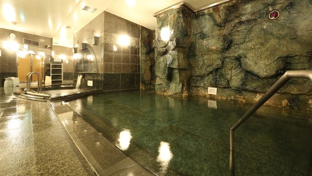 Une piscine intérieure moderne, avec un mur de fond en pierre, une eau cristalline et un escalier en métal.