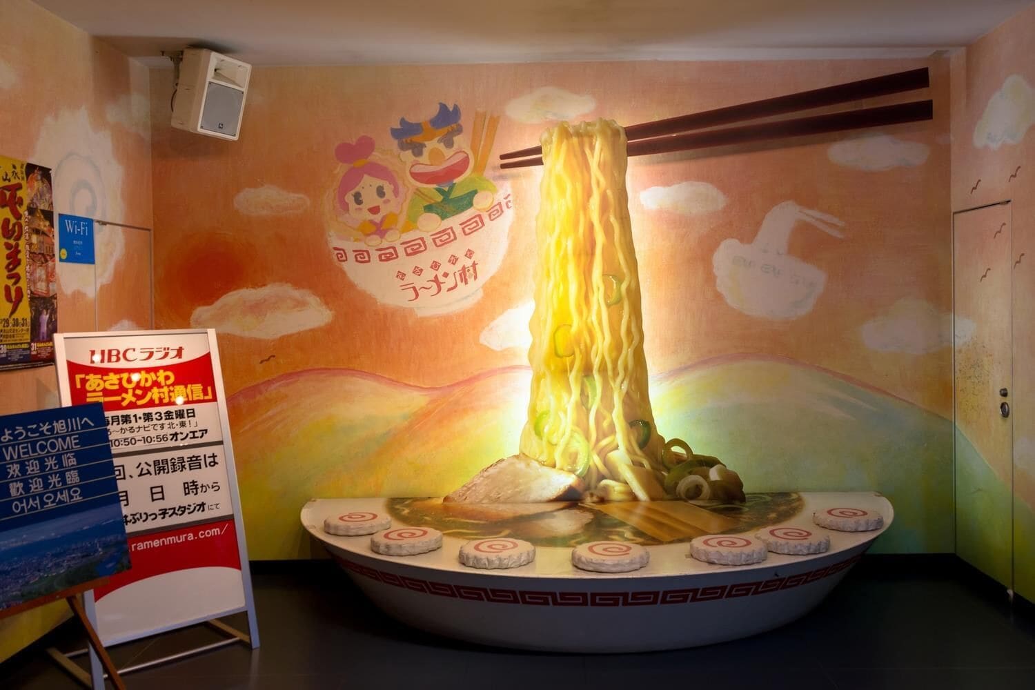 A ramen restaurant with a large bowl of ramen in the center, surrounded by chopsticks and a bowl of soup.