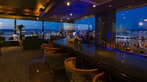 Un bar offrant une vue panoramique sur la ville, doté de tabourets et proposant un large choix de bouteilles.