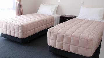Deux lits simples avec des têtes de lit, une table de chevet et une prise électrique murale.