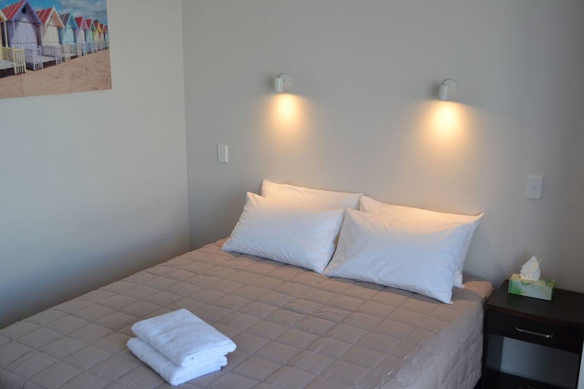 A neatly made bed with white linens, two wall-mounted lights, and a bedside table with a tissue box.