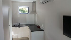 A compact kitchen with white cabinets, a black countertop, a window, and an air conditioning unit. - 319 Addington Motel (Christchurch)
