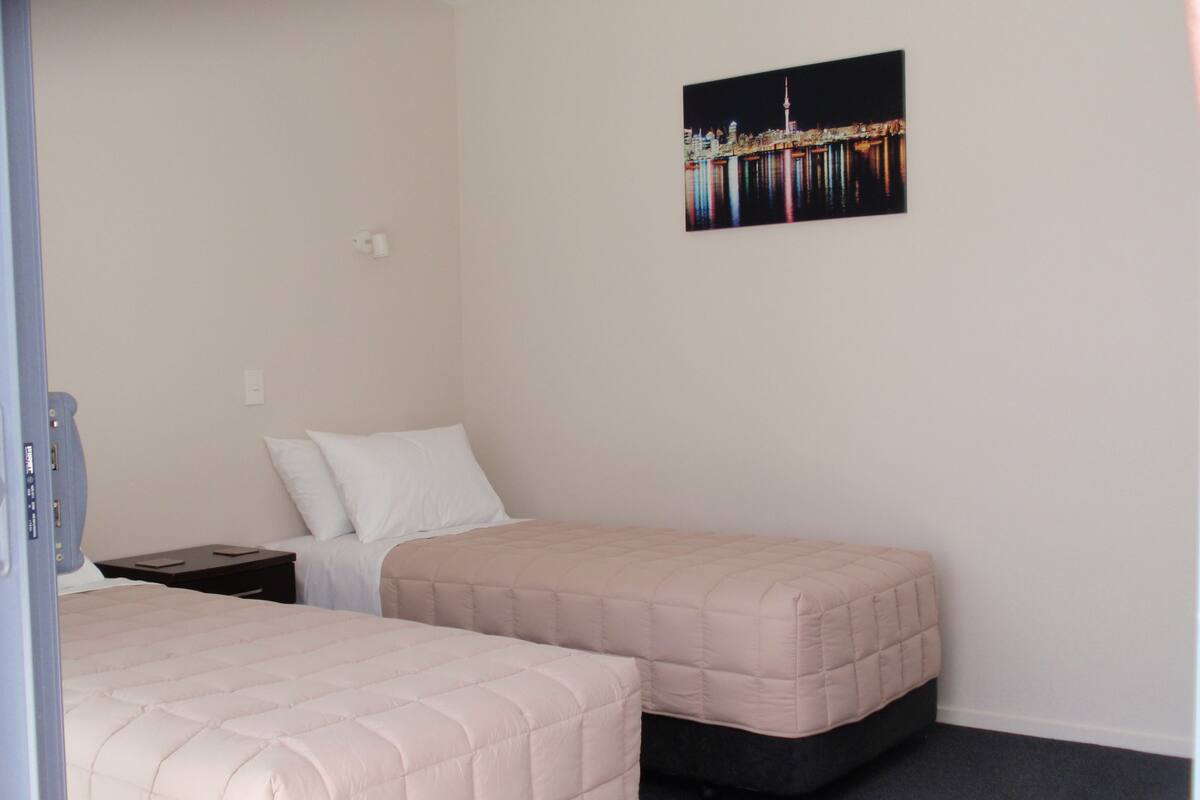 A hotel room with two beds, a nightstand, and a wall-mounted picture.
