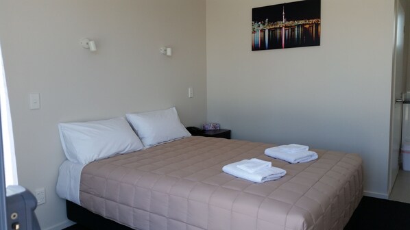 A neatly made bed with a beige quilt, two white pillows, and two folded white towels on the bed.