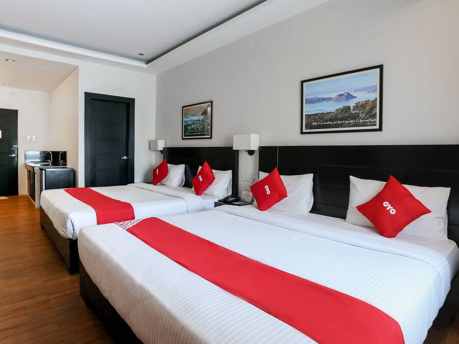 A hotel room with two beds, each with white bedding and red accents, a black headboard, a framed landscape picture on the wall, and a wooden floor.