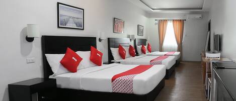 A hotel room with three beds, each with red and white bedding, a desk with a chair, a TV, and a window with curtains.