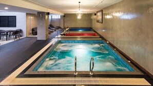Una piscina con varias pistas de natación, un área de descanso con sillas y un accesorio de iluminación en el techo.