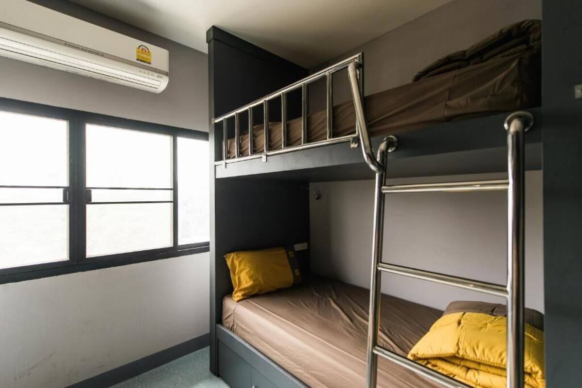 A bunk bed room with a window, an air conditioning unit, and a metal ladder.