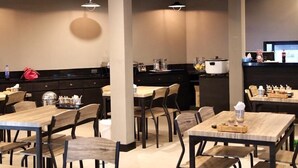 Un interior de restaurante moderno con mesas y sillas de madera, una barra con electrodomésticos de cocina e iluminación colgante.