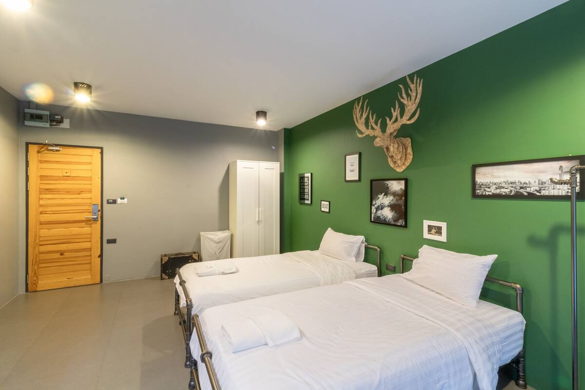 A hotel room with two beds, a green wall, a wooden door, and a deer head decoration.