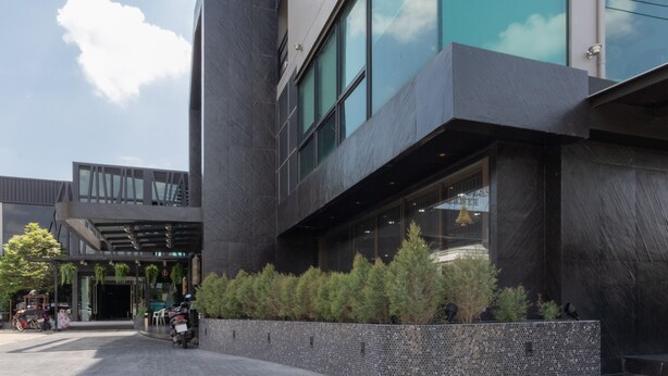 Un edificio moderno con fachada oscura, ventanas amplias y un área de entrada cubierta con asientos.
