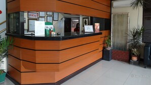 A reception desk with a modern design, featuring a glass partition and a black countertop. There are several informational posters and a green directory stand on the desk. - RueMango Apartelle and Suites (Davao)