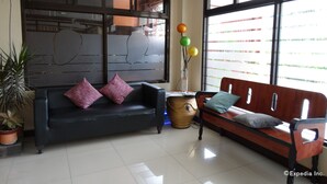 A modern living room with a dark sofa, a wooden bench, and a potted plant. - RueMango Apartelle and Suites (Davao)