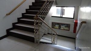 A staircase with black steps and a white handrail, leading to a landing with a window and a framed picture. - RueMango Apartelle and Suites (Davao)