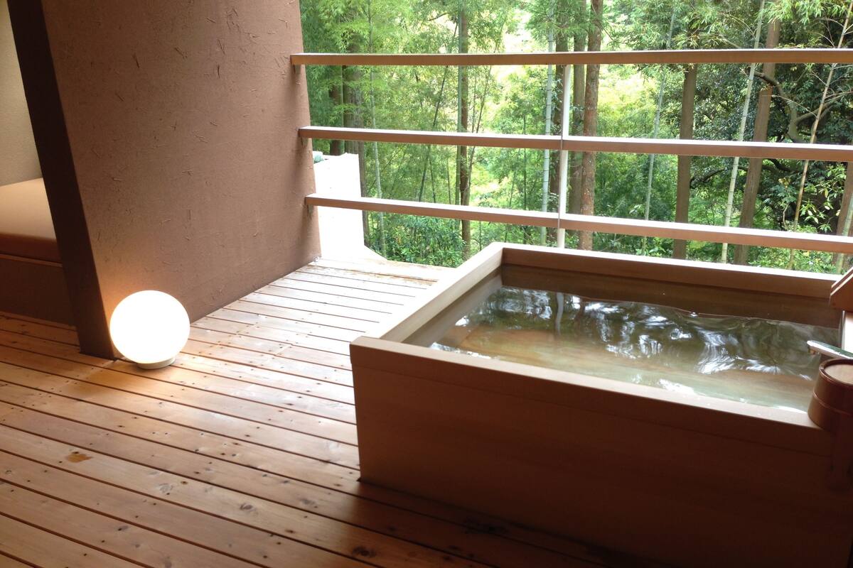 A wooden deck with a hot tub and a window overlooking a forest.