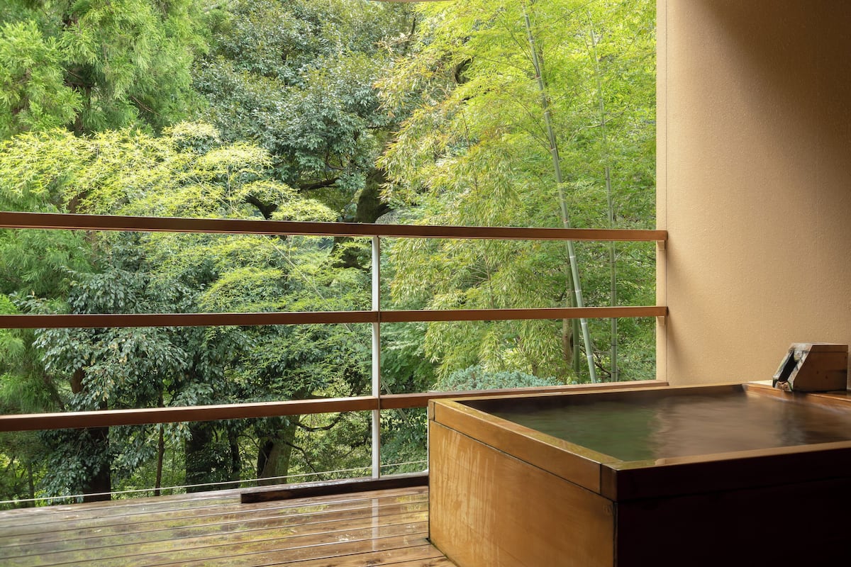 A room with a wooden deck, a hot tub, and a large window overlooking a forest.