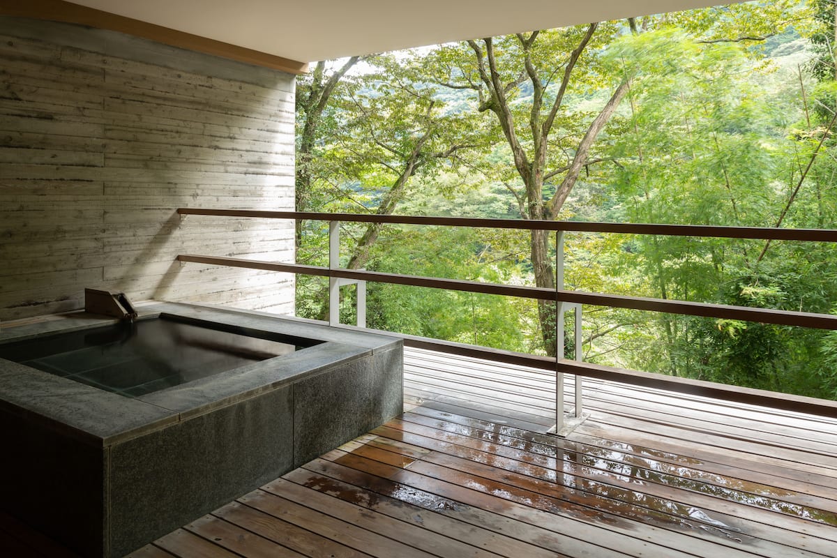A spa area with a stone hot tub and a wooden deck overlooking a forest.