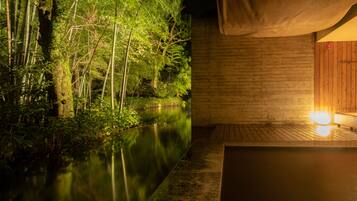 A serene indoor setting with a wooden deck overlooking a calm water body, surrounded by lush greenery.
