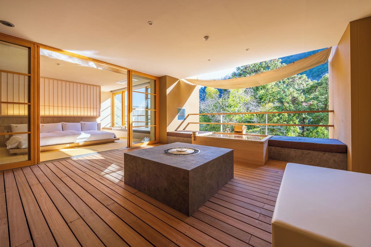 A modern, open-plan room with a wooden floor, a large window, and a view of greenery.