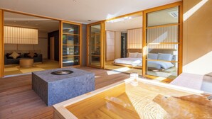 A modern hotel room with a wooden floor, a stone accent piece, a wooden bathtub, and a sliding glass door leading to a balcony. - Kinnotake Tonosawa - Adult Only (Hakone)