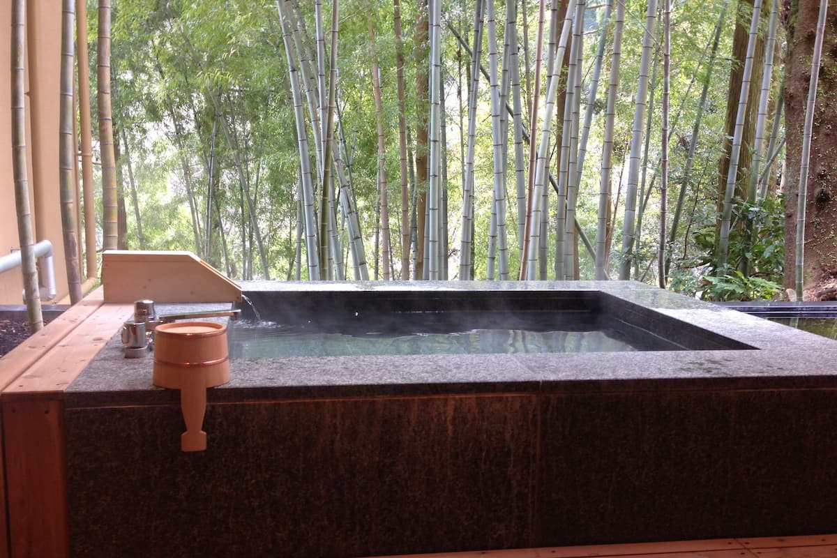 A hot tub with a wooden deck and a view of bamboo trees.