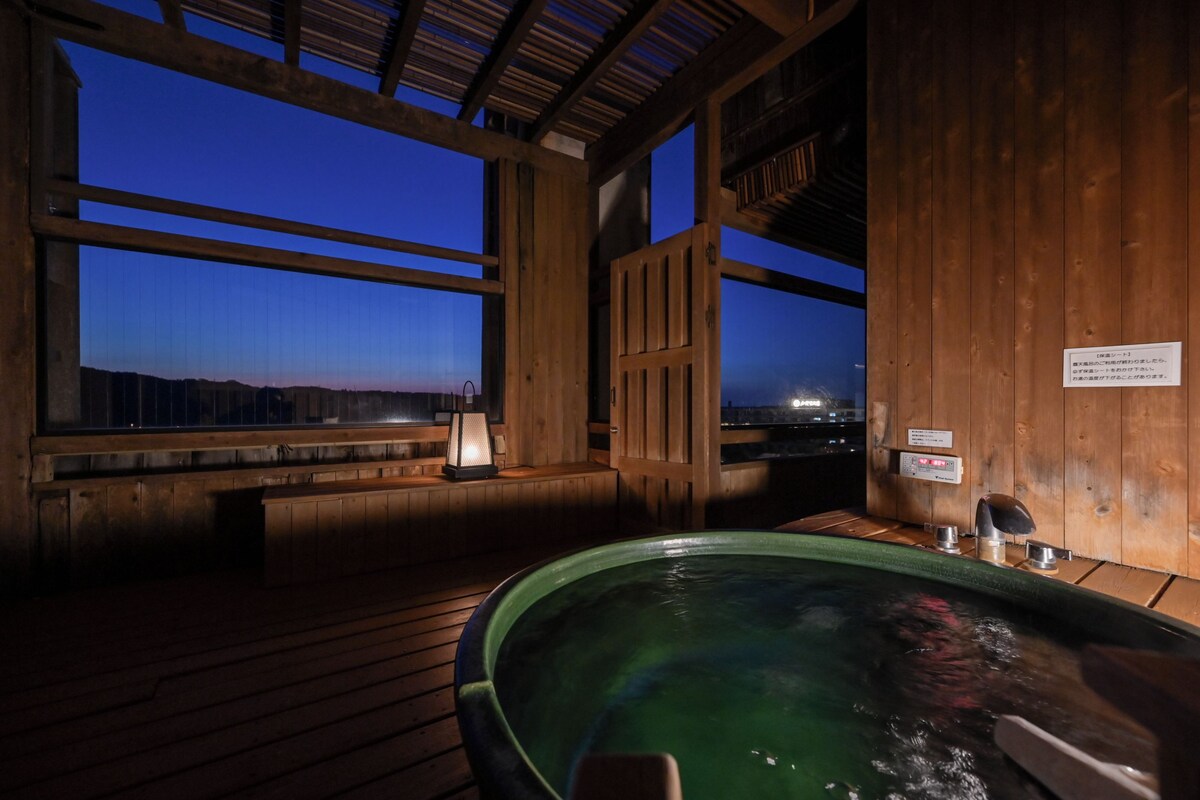 Ein hölzerner Wellnessbereich mit Whirlpool, Holzliegen und Blick auf die Berge im Abenddämmerung.