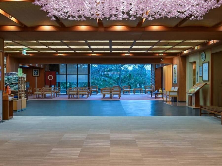 Un hall espacioso con suelo de madera, techo decorado con motivos florales y vistas a árboles a través de amplias ventanas.