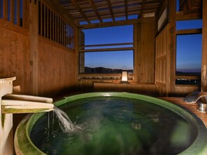 A wooden spa room with a hot tub, a wooden bench, and a view of the mountains at dusk.