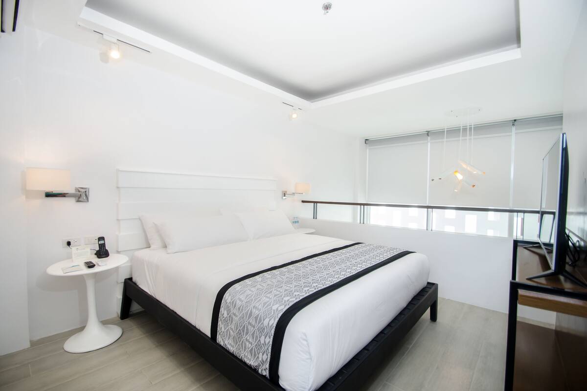A modern hotel room with a large bed, bedside tables, a desk, and a large window with a view.