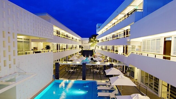 Un hotel moderno con zona de piscina central, varios balcones y mobiliario exterior.