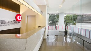 A modern reception area with a marble counter, a large illuminated logo, and a glass partition. - Amaris Hotel Setiabudhi (Bandung)