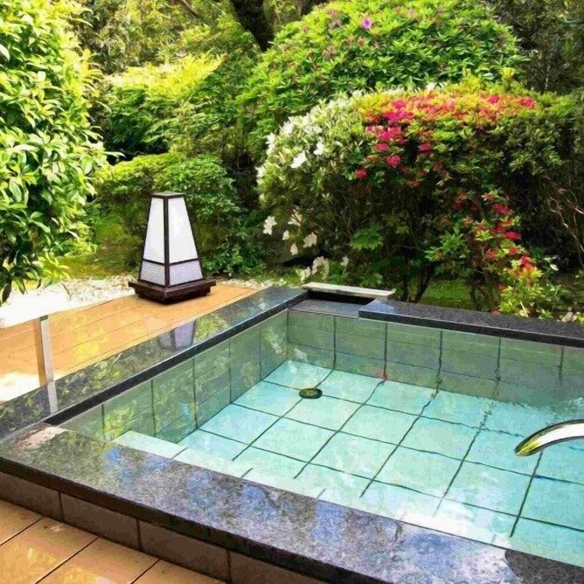A rectangular pool with a tiled edge, surrounded by lush greenery and a decorative lamp.
