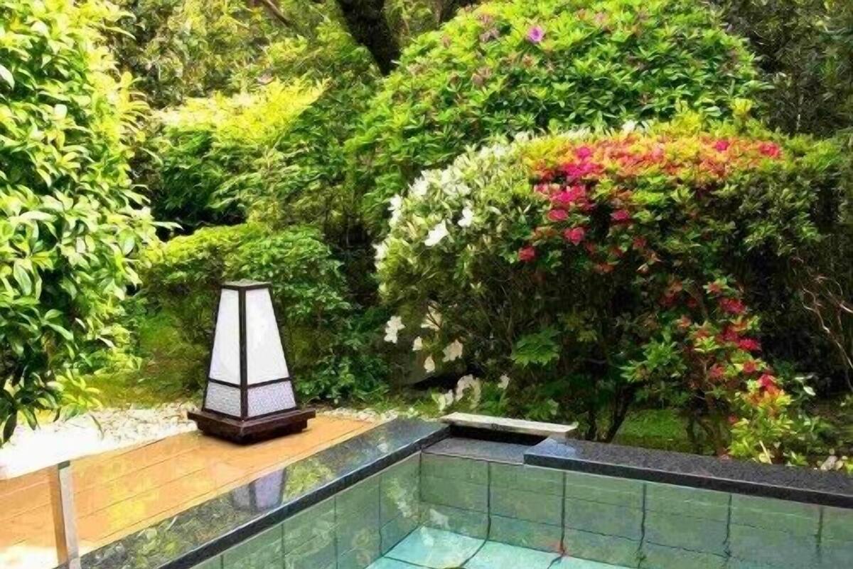 A rectangular pool with a tiled edge, surrounded by lush greenery and a decorative lamp.
