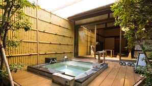 En træterrasse med jacuzzi, bambusvæg og en glasdør, der fører til et indendørsrum.