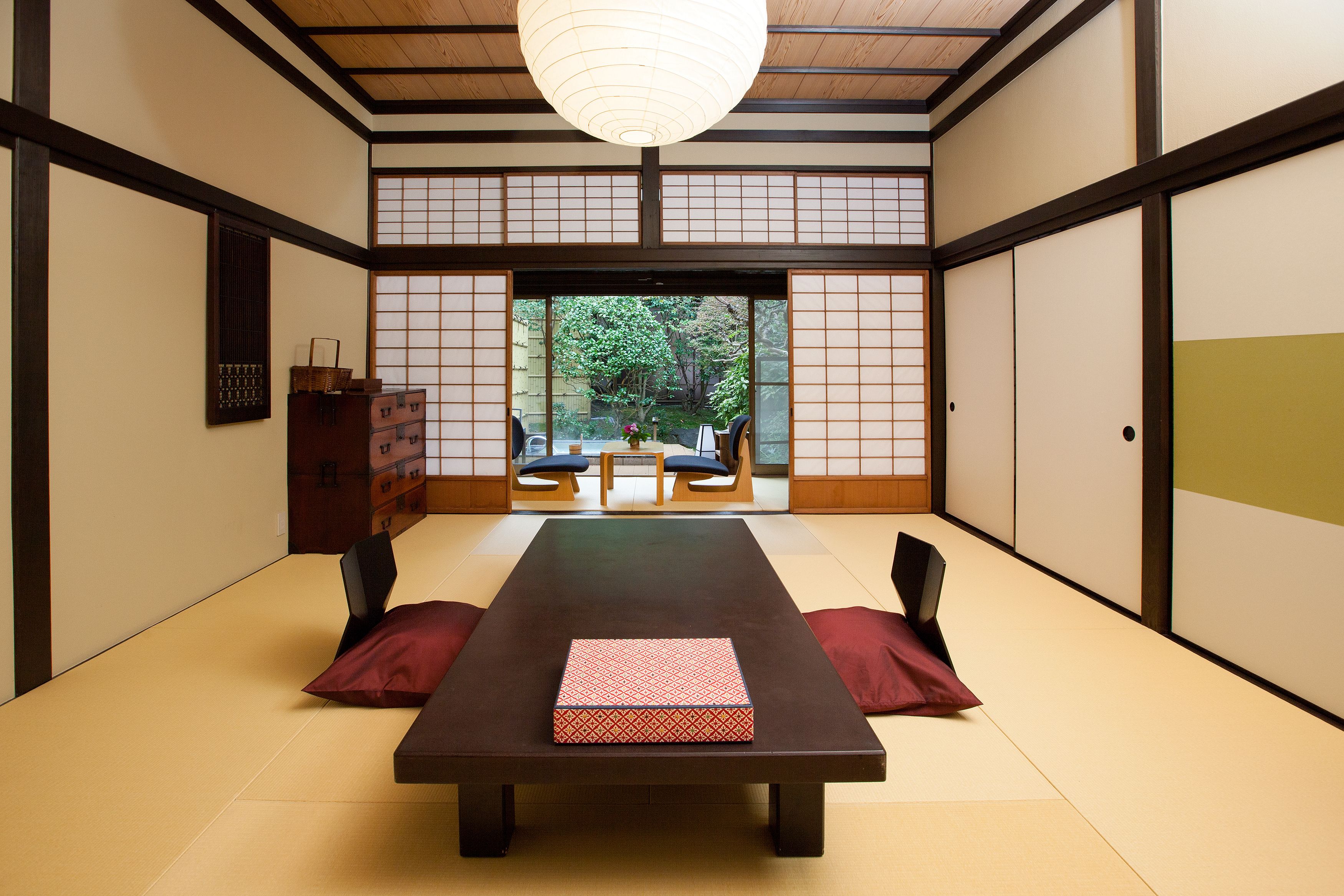 A traditional Japanese room with tatami flooring, a low table with a red patterned mat, and sliding doors leading to an outdoor seating area.