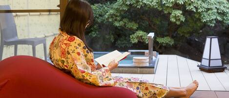 A person sitting on a red bean bag chair reading a book in a room with a wooden floor and a view of greenery outside.