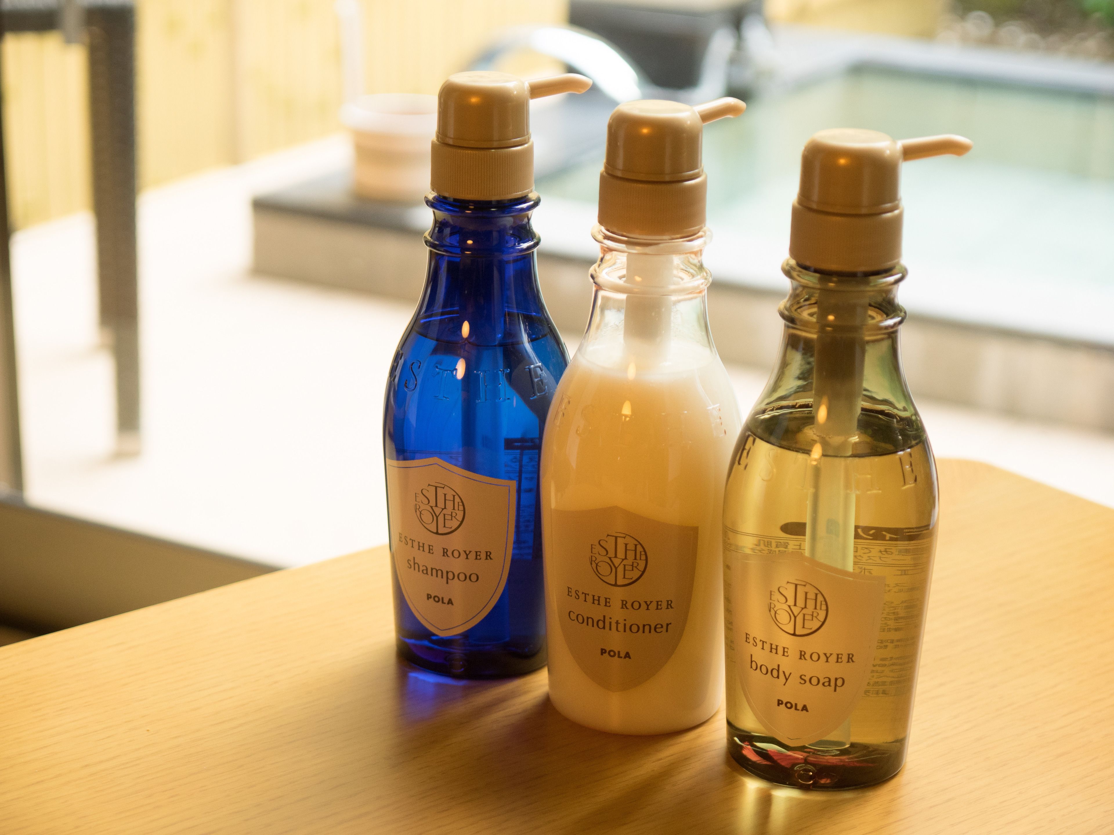 Tres botellas de productos para el cuidado corporal ESTHE ROYER sobre una mesa de madera.