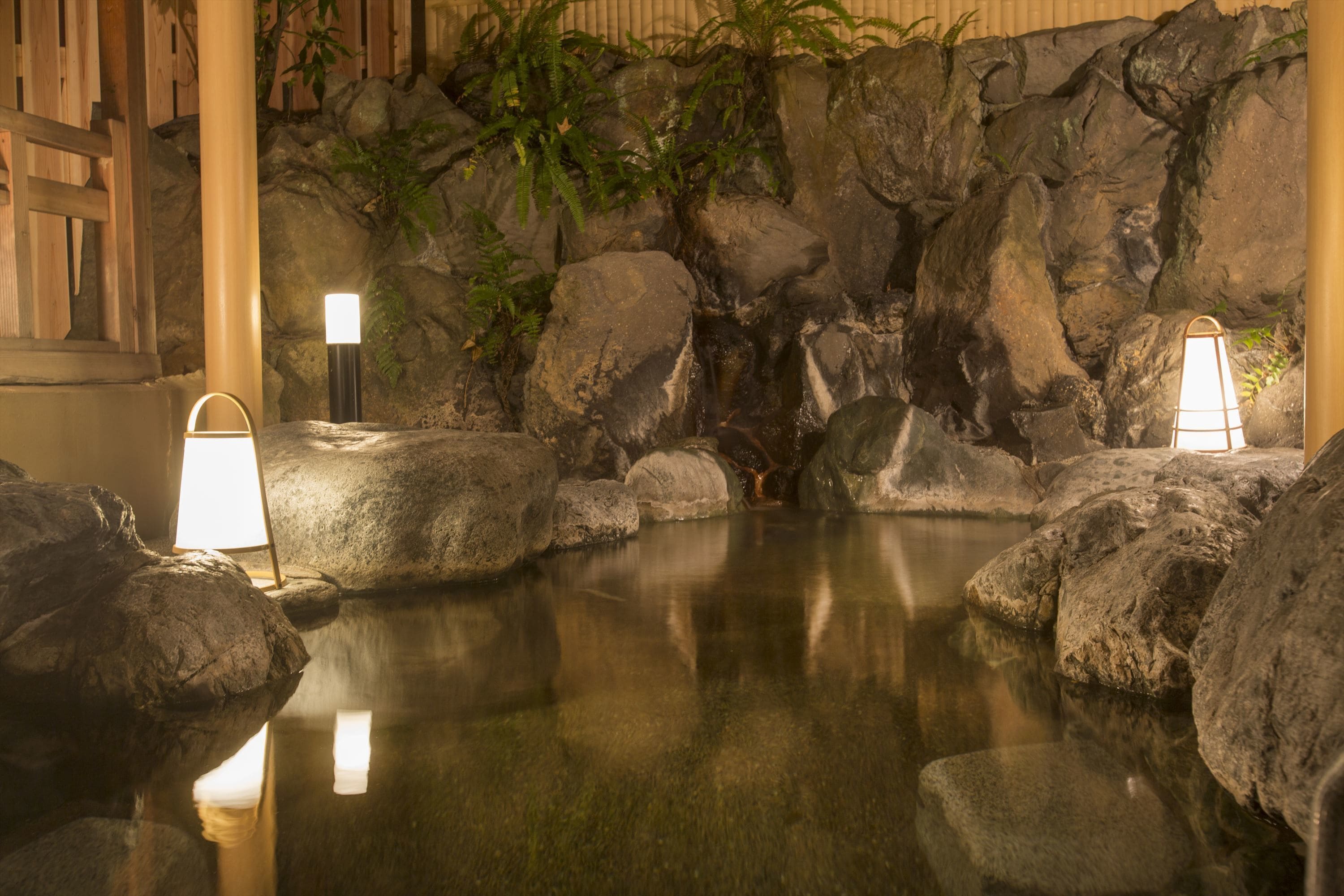 A tranquil indoor water feature with rocks and plants, illuminated by two wall-mounted lights.