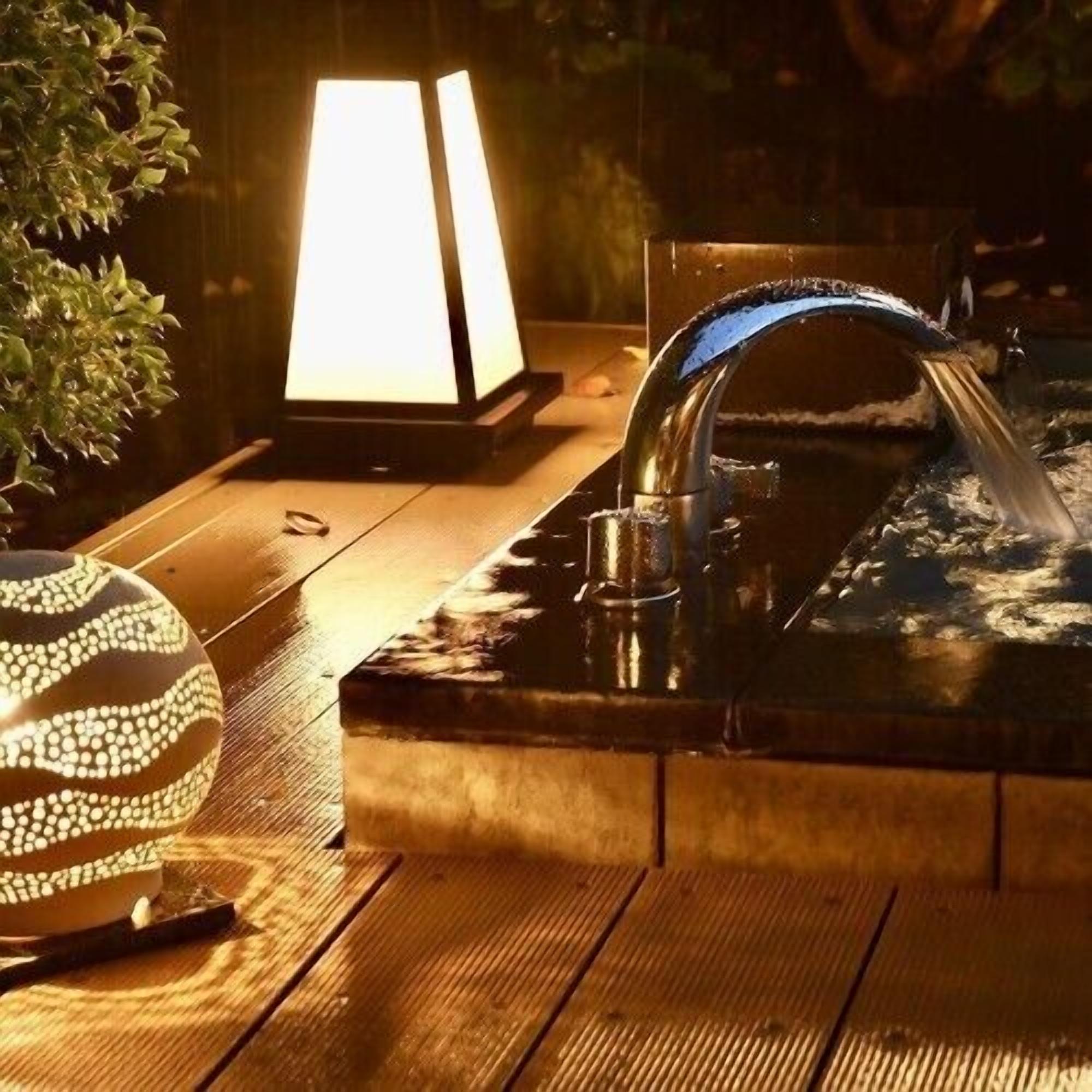 A wooden table with a decorative bowl, a lit lamp, and a water feature.