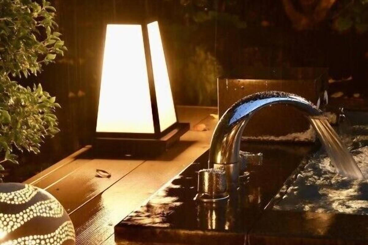 A wooden table with a decorative bowl, a lit lamp, and a water feature.